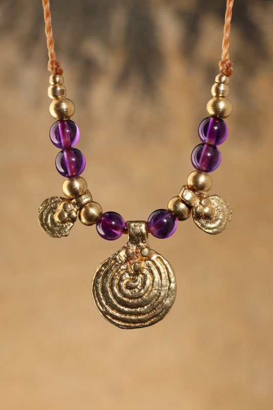 Halskette mit Edelstein- und Messingperlen sowie 3 runden Messinganhängern. Zentraler Messinganhänger mit Spiralsymbol. Kette aus beigem Makrameegarn. Stein und Farbe: Amethyst –lila/klar. Für Affirmation: „Ich bin easy“