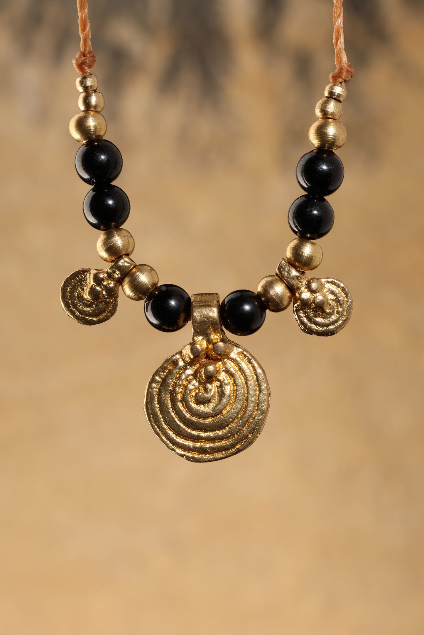 Halskette mit Edelstein- und Messingperlen sowie 3 runden Messinganhängern. Zentraler Messinganhänger mit Spiralsymbol. Kette aus beigem Makrameegarn. Stein und Farbe: Turmalin –schwarz. Für Affirmation: „Ich bin safe“