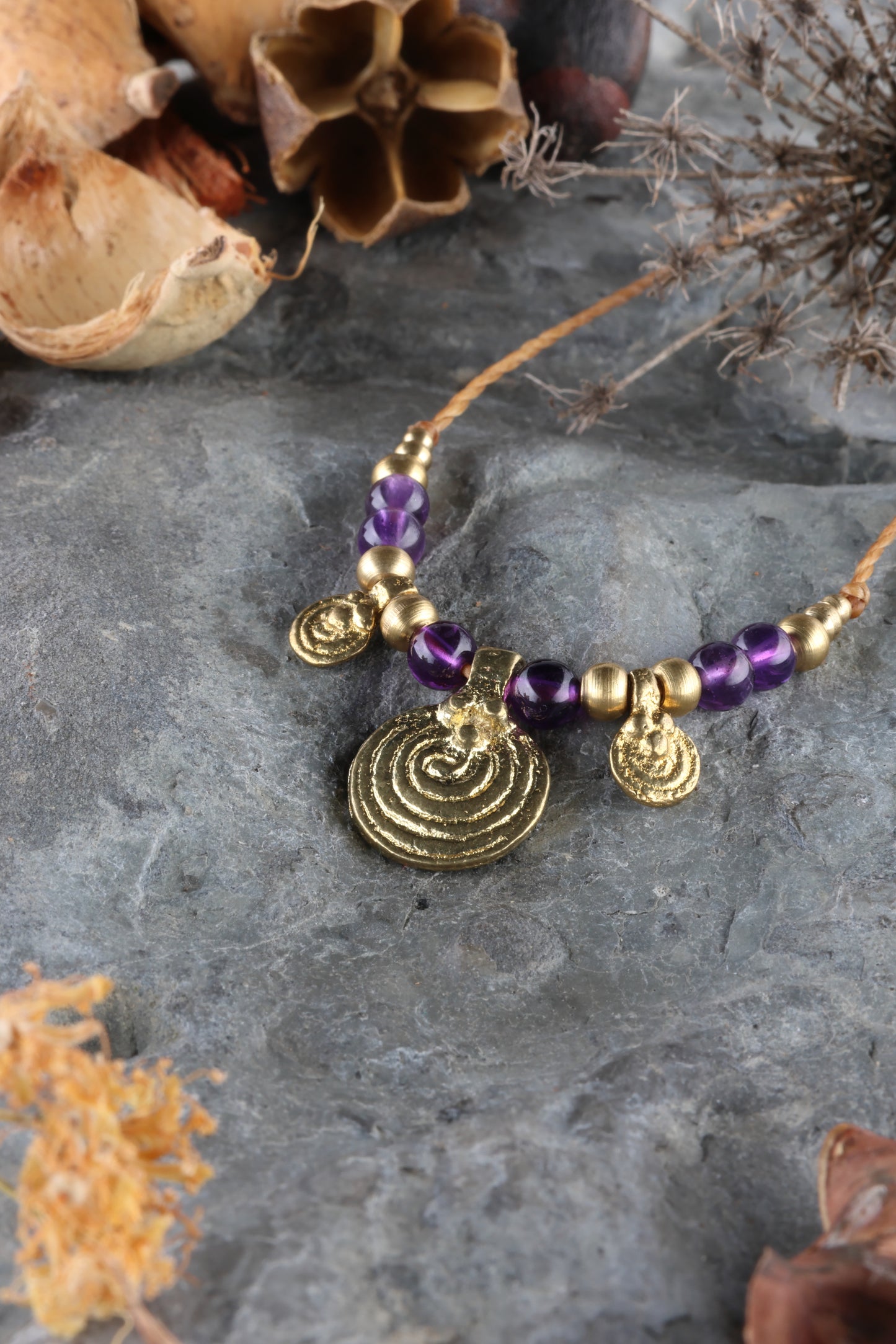 Halskette mit Edelstein- und Messingperlen sowie 3 runden Messinganhängern. Zentraler Messinganhänger mit Spiralsymbol. Kette aus beigem Makrameegarn. Stein und Farbe: Amethyst –lila/klar. Für Affirmation: „Ich bin easy“