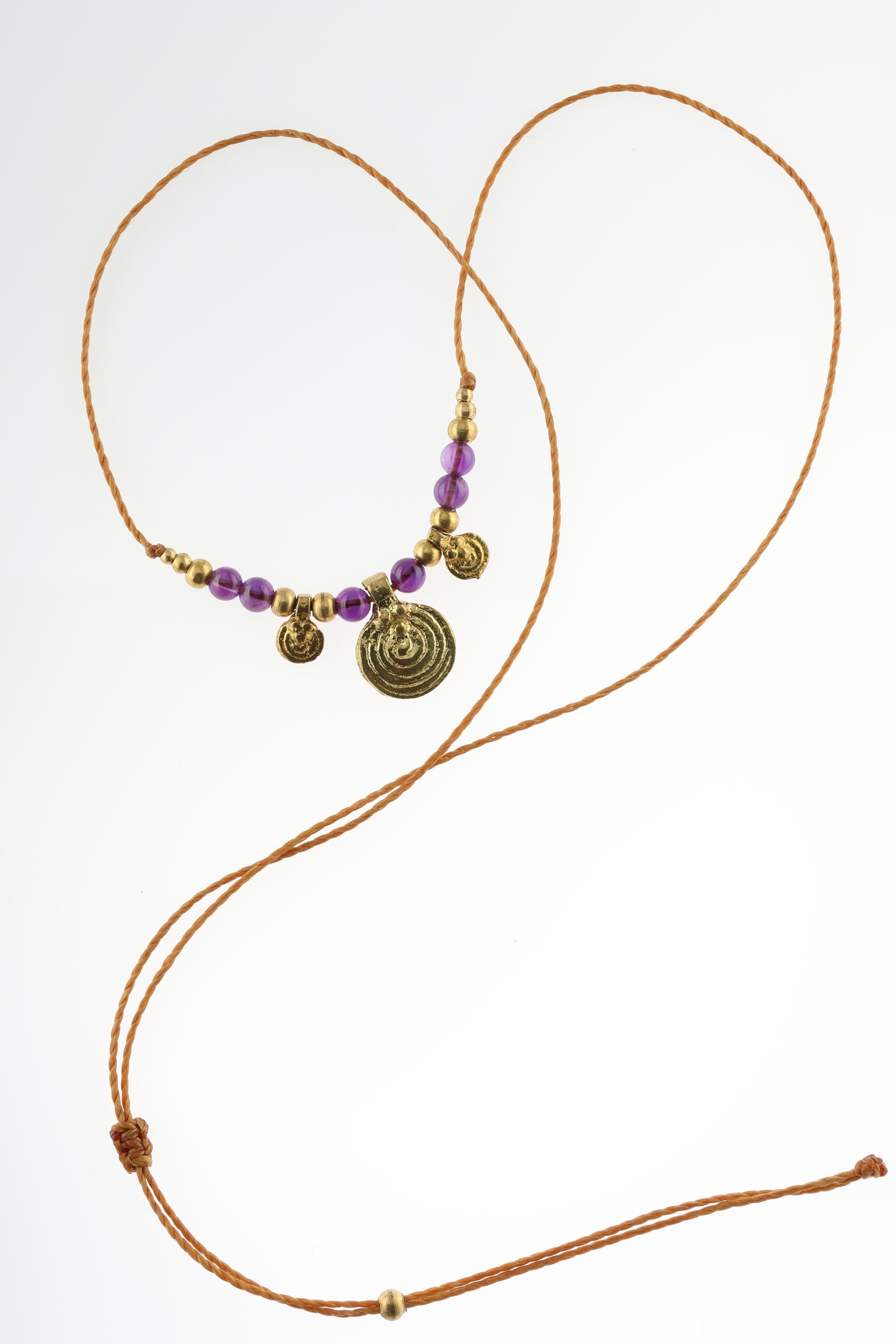 Halskette mit Edelstein- und Messingperlen sowie 3 runden Messinganhängern. Zentraler Messinganhänger mit Spiralsymbol. Kette aus beigem Makrameegarn. Stein und Farbe: Amethyst –lila/klar. Für Affirmation: „Ich bin easy“