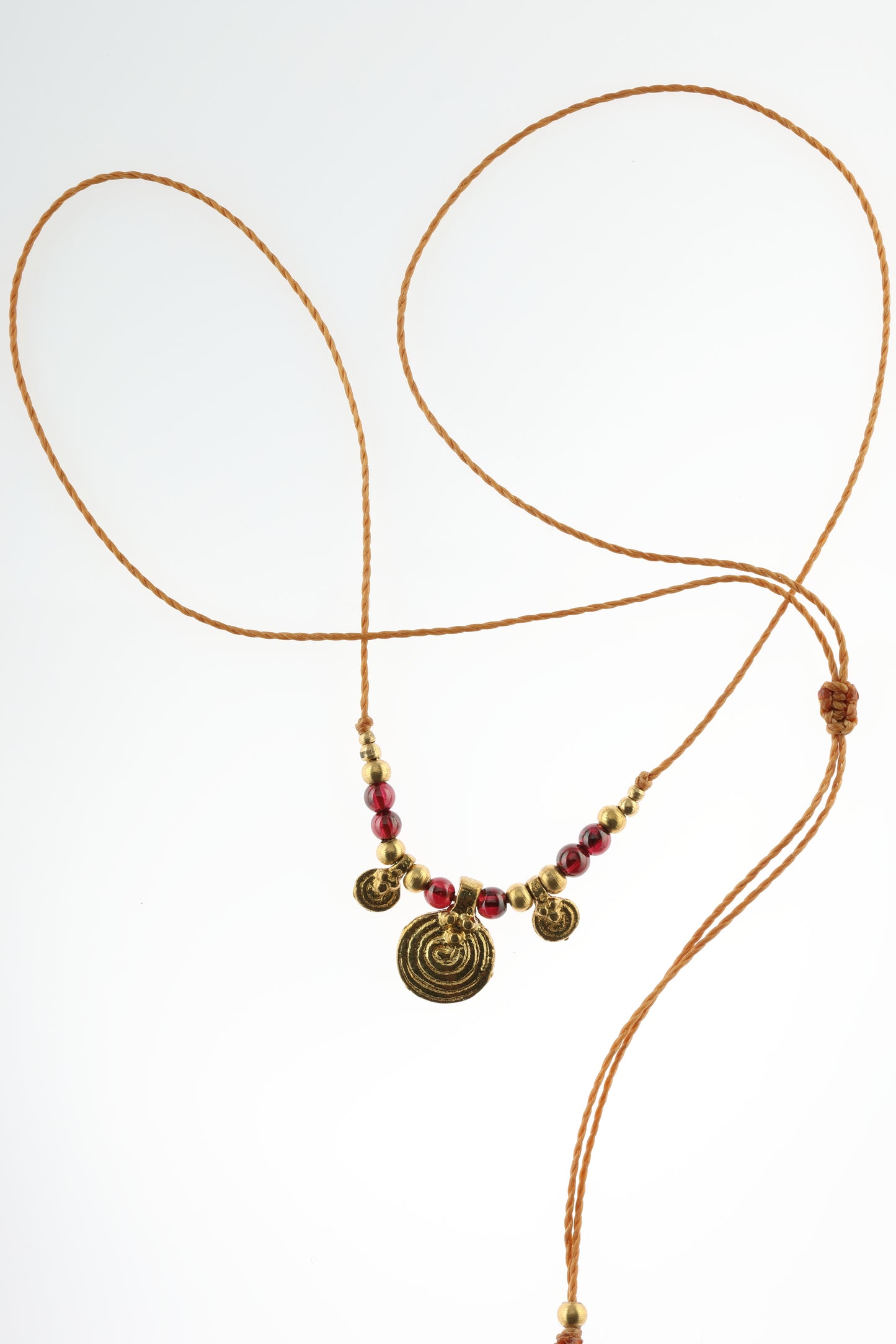 Halskette mit Edelstein- und Messingperlen sowie 3 runden Messinganhängern. Zentraler Messinganhänger mit Spiralsymbol. Kette aus beigem Makrameegarn. Stein und Farbe: Granat –dunkelrot/klar. Für Affirmation: „Ich bin mutig“