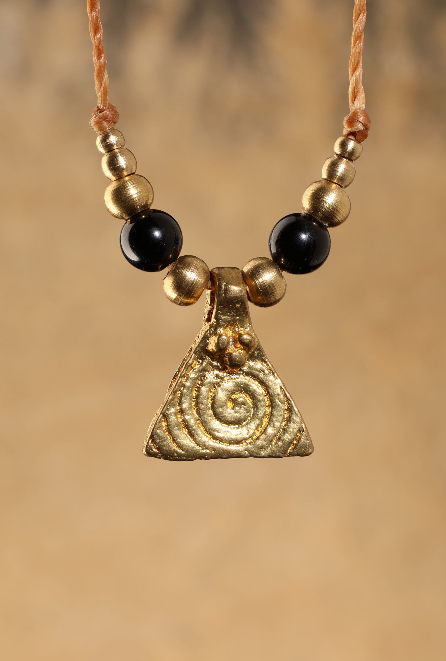 Halskette mit Edelstein- und Messingperlen sowie einem dreieckigen Messinganhänger mit Spiralsymbol. Kette aus beigem Makrameegarn. Stein und Farbe: Turmalin –schwarz. Für Affirmation: „Ich bin safe“