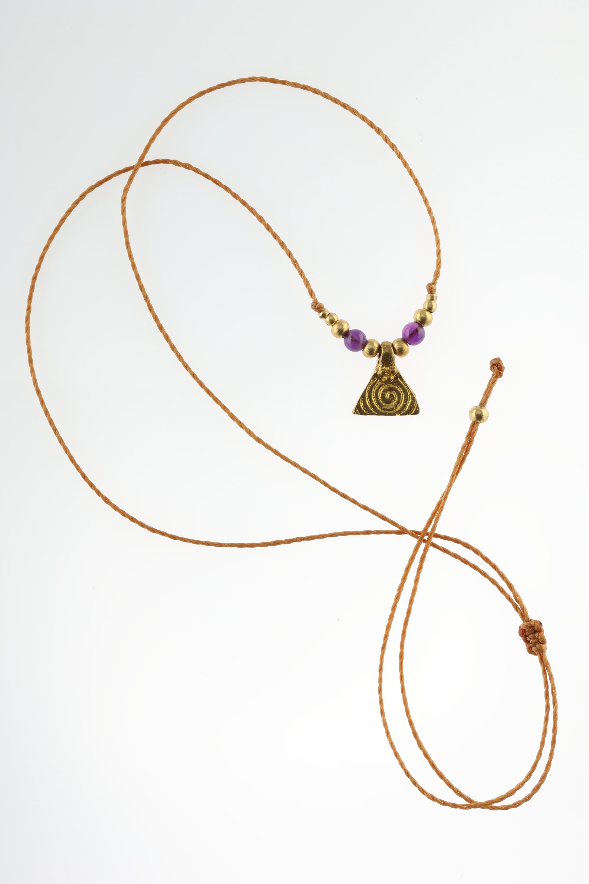 Halskette mit Edelstein- und Messingperlen sowie einem dreieckigen Messinganhänger mit Spiralsymbol. Kette aus beigem Makrameegarn. Stein und Farbe: Amethyst – lila/klar. Für Affirmation: „Ich bin easy“