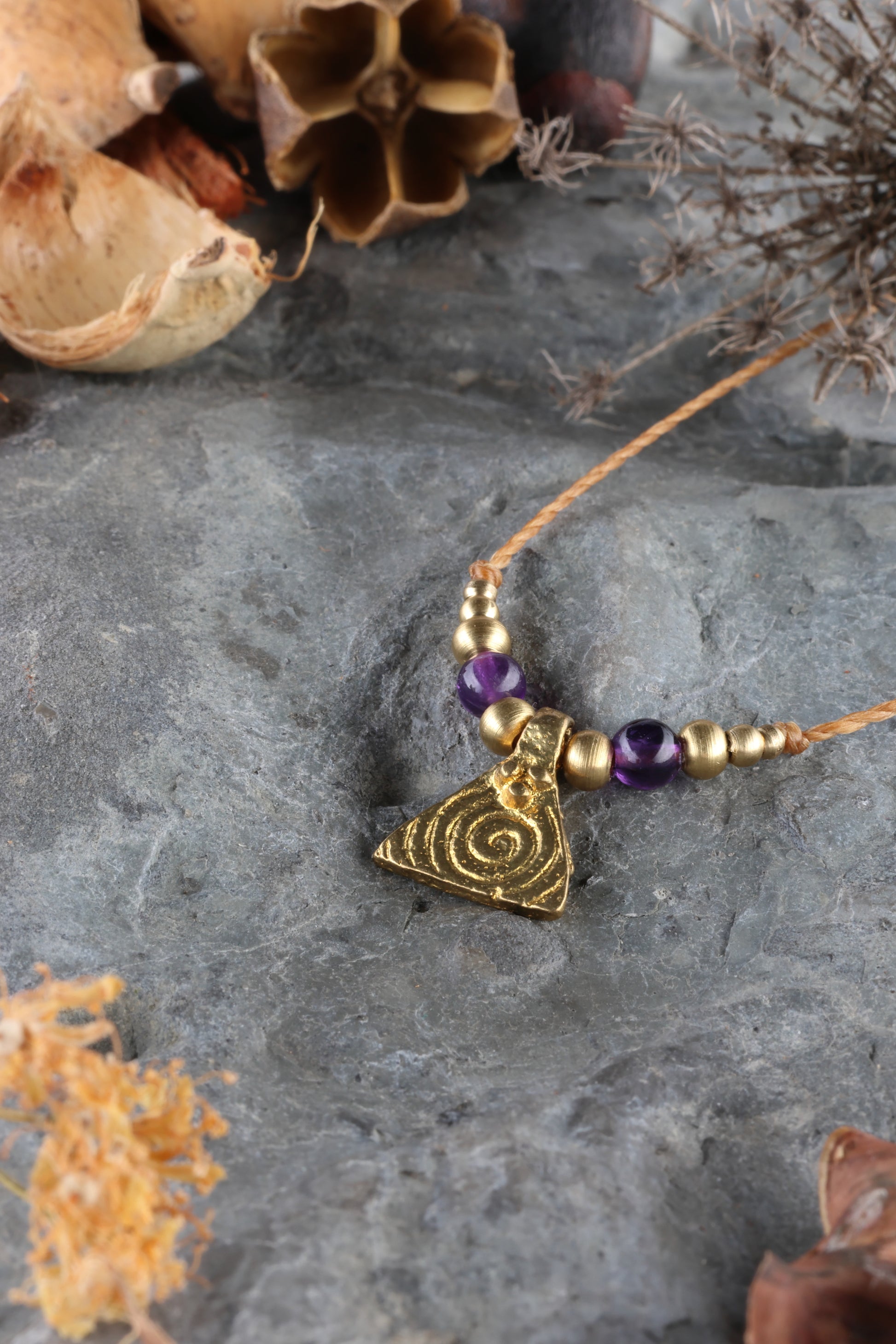 Halskette mit Edelstein- und Messingperlen sowie einem dreieckigen Messinganhänger mit Spiralsymbol. Kette aus beigem Makrameegarn. Stein und Farbe: Amethyst – lila/klar. Für Affirmation: „Ich bin easy“