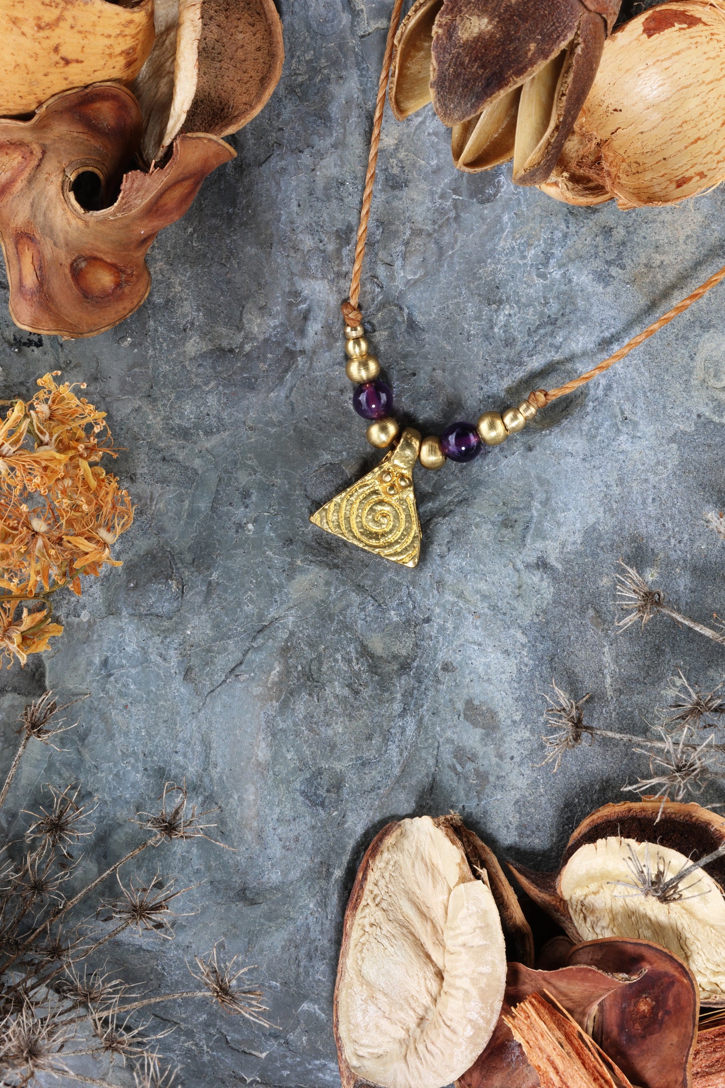 Halskette mit Edelstein- und Messingperlen sowie einem dreieckigen Messinganhänger mit Spiralsymbol. Kette aus beigem Makrameegarn. Stein und Farbe: Amethyst – lila/klar. Für Affirmation: „Ich bin easy“