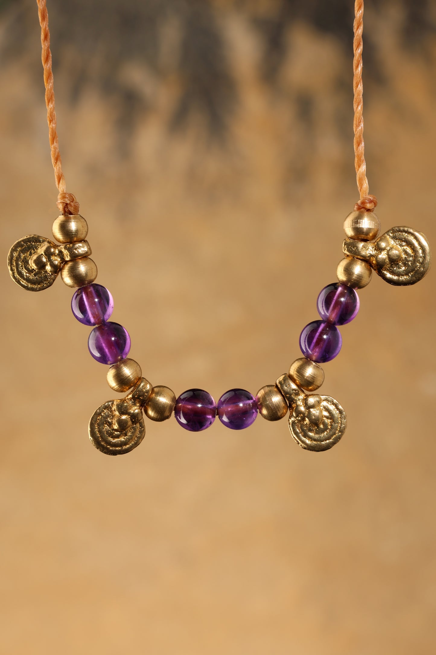 Halskette mit Edelstein- und Messingperlen sowie 4 kleinen runden Messinganhängern. Kette aus beigem Makrameegarn. Stein und Farbe: Amethyst – lila/klar. Für Affirmation: „Ich bin easy“