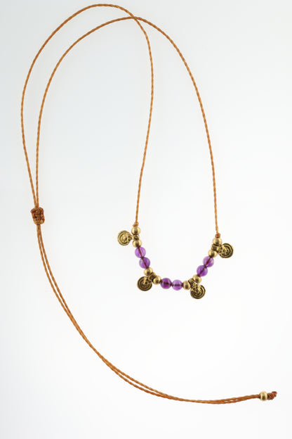 Halskette mit Edelstein- und Messingperlen sowie 4 kleinen runden Messinganhängern. Kette aus beigem Makrameegarn. Stein und Farbe: Amethyst – lila/klar. Für Affirmation: „Ich bin easy“