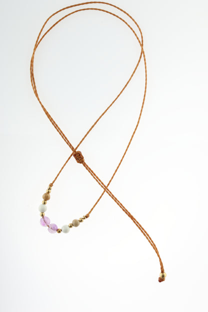 Halskette mit Edelstein- und Messingperlen an beigem Makrameegarn. Steine und Farbe: Versteinertes Holz – braun, Magnesit – weiß, Amethyst - lila. Für Sternzeichen: Wassermann